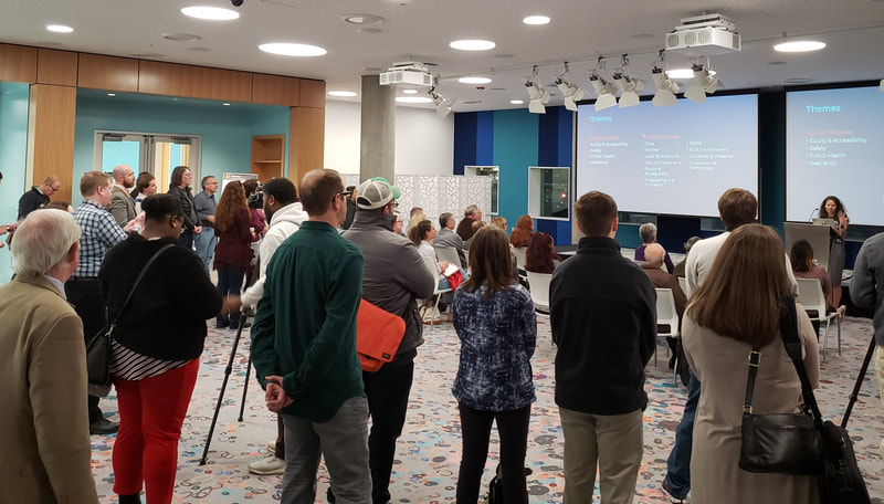 Presentation at Richland Library Main - image of citizens gathered, standing and sitting, with their attention focused on a screen and speaker at the front of the room