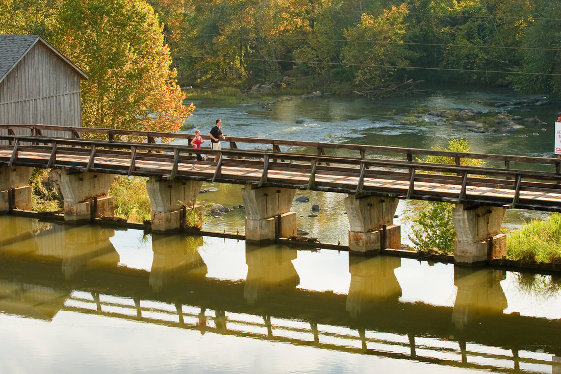 Photograph of a man and a woman running along the riverfront park bridge with the Columbia Canal in the foreground.